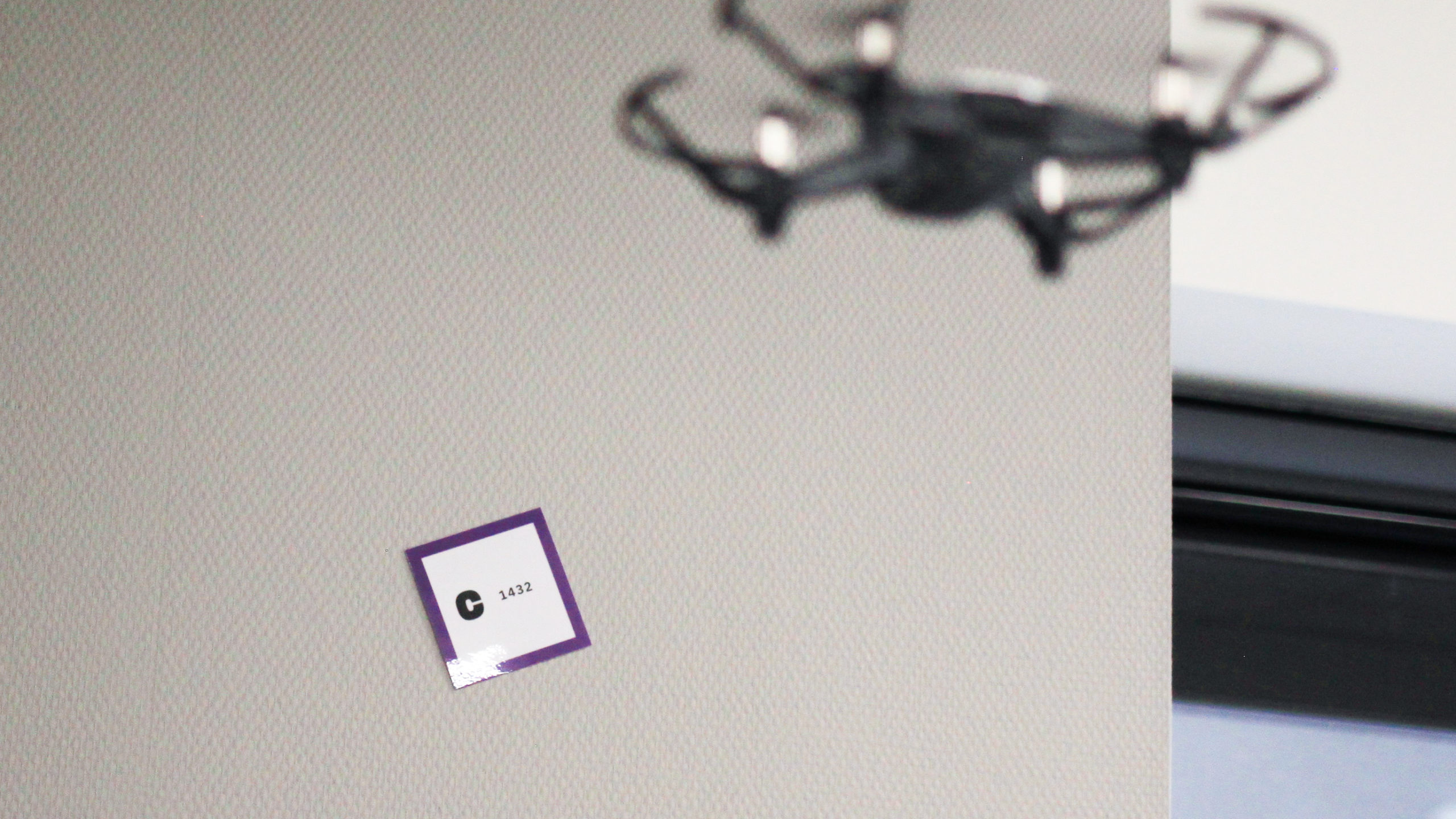 Photographie d'un petit drone en vol, faisant face à un code collé sur un mur.